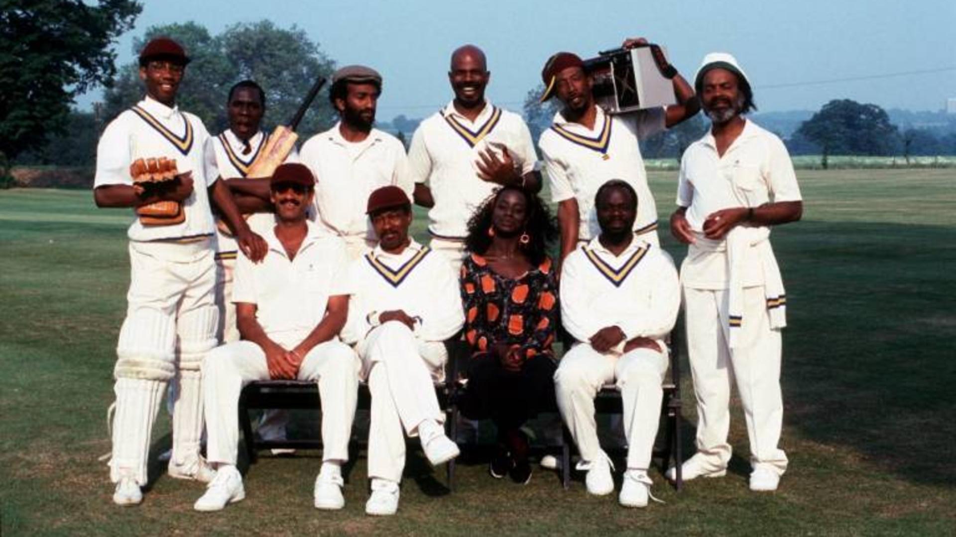 Still from Playing Away. Ten people in cricket attire and equipment pose for a group portrait in a cricket field.