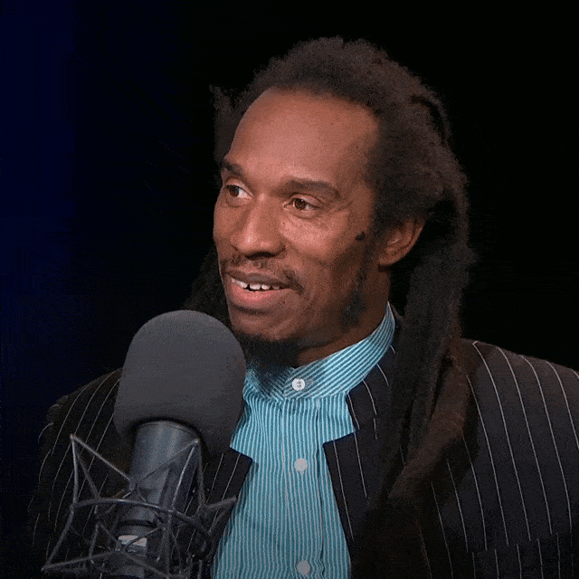 Moving image of Benjaming Zephaniah in pinstripe suit, speaking into a microphone, with the subtitle: &ldquo;I&rsquo;d like to have a revolution, but everybody&rsquo;s too busy shopping.&rdquo;